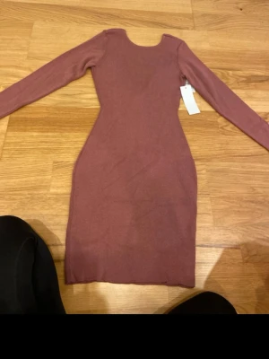 Rosa stickad långärmad klänning - Supersnygg rosa stickad klänning med lång ärm och figurnära passform. Klänningen har en enkel design med rund halsringning och är gjord i mjukt material som känns skönt mot huden. Perfekt för dig som gillar stilrena plagg med en feminin touch. V ringad i ryggen 