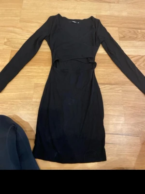 Svart ribbad cut out klänning Bik Bok - Säljer en svart ribbad kortklänning från Bik Bok i storlek XS. Klänningen har lång ärm, v-ringning och en snygg cut out-detalj i midjan som ger en trendig look. Perfekt för dig som gillar stilrena och moderna plagg.