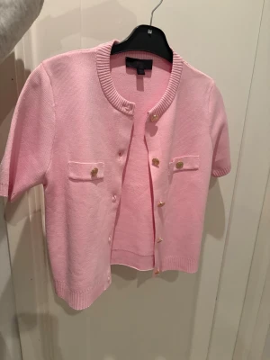 Zara stickad jacka med kort ärm - Rosa topp/kofta från Zara i storlek S. Köpt för 399 kr och säljs inte längre i butik. Aldrig använd, i nyskick. Snygga guldfärgade knappar och mjukt material. Perfekt både till vardag och finare tillfällen. Se bilder för detaljer.
