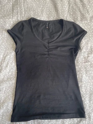 Svart topp med v-ringning från Track - En svart topp från Track i storlek S. Modellen har v-ringning med rynkdetalj framtill och korta ärmar. Tillverkad i mjuk bomull som känns skön mot huden. Enkel och stilren design som passar till många olika looks. Passar mig xxs/xs ta gärna emot bud och frågor💕😊