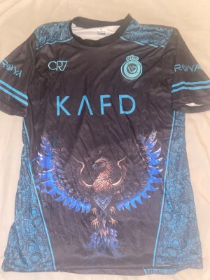 CR7 t-shirt - En CR7 t-shirt med färgen svart, blå, med en örn i mitten på tröjan. Nytt pris 549kr