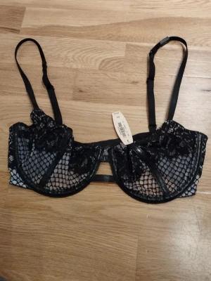 NY Svart spets-bh från Victoria's Secret - Säljer en svart bh från Victoria's Secret med snygga spetsdetaljer och nätmönster. Justerbara axelband och bygel för extra stöd. Perfekt för dig som vill ha något både stilrent och edgy. Storlek 32D vilket är som 70D, kan passa en större C också. Perfekt för alla hjärtans dag  / Valentine's day. Jag har fler annonser uppe och ger mängd rabatt, så kolla gärna min sida!