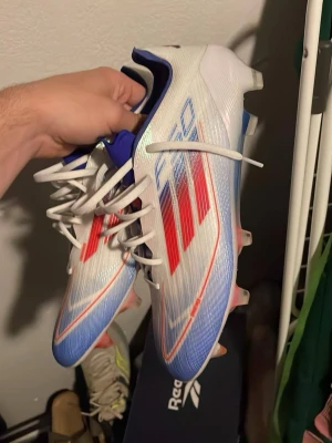 Adidas F50 Elite FG fotbollsskor - Säljer ett par Adidas F50 Elite FG fotbollsskor i vitt med röda och blå detaljer. Endast testade ca 10 min. Extra sulor följer med samt originalkartong.