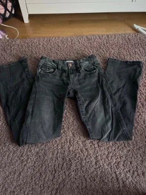 Svarta bootcut jeans i strl 158 - Säljer ett par mörk gråa bootcut jeans från Gina Tricot i storlek 158. Jeansen har detaljerade fickor och är justerbara i midjan!