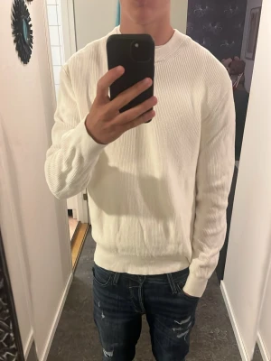 Vit stickad långärmad tröja - Klassisk vit stickad tröja med lång ärm och ribbade muddar från hm. Enkel och clean design som passar till allt. Mjuk och skön känsla, perfekt för lager på lager under kyligare dagar. Sitter bra på mig som är 180, bara att höra av sig vid frågor!
