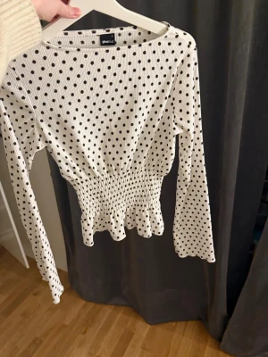 Prickig långärmad topp Gina Tricot - Använd en gång, Supersöt vit långärmad topp från Gina Tricot med svarta prickar. Toppen har ribbad struktur, smockad midja och volangkant nedtill som ger en feminin siluett. Perfekt att styla med jeans eller kjol för en trendig look.