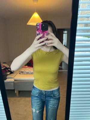 Gul croppad topp med rynkad krage - Säljer en gul croppad topp med korta ärmar och en snygg rynkad detalj vid kragen. Toppen är figurnära och gjord i mjukt bomullsmaterial, perfekt till jeans eller kjol. Enkel men ändå unik med sin fina krage.