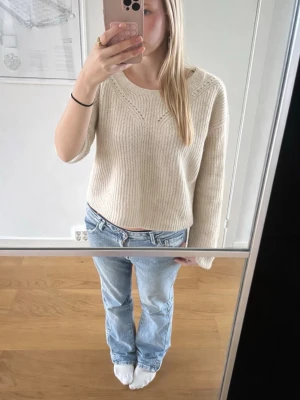 Beige stickad tröja från H&M - Mysig beige stickad tröja från H&M med rund halsringning och diskret ribbad struktur. Tröjan har en något croppad passform och långa ärmar, perfekt att styla med jeans för en chill look. Den är kortare i magen än vad det igentligen ser ut som på bilden