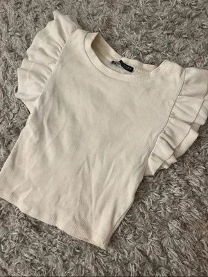 Vit ribbad topp med volangärmar - Säljer en söt vit topp från Zara med korta ärmar med volanger.