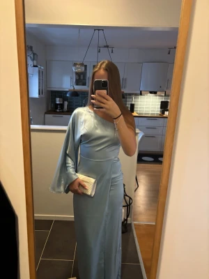 Ljusblå balklänning - Säljer en ljusblå balklänning från adoore i satinliknande material. Klänningen har en axelbandslös design med en vid, lång ärm på ena sidan. OBS klänningen är utsydd till en 36 av skräddare och är alltså inte en 34 längre (se näst sista bilden i sidan). Lapp är fortfarande kvar💕