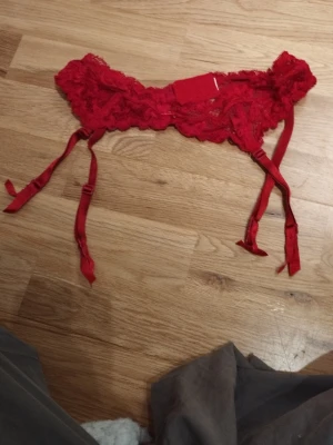 Röd spets strumpebandhållare - Säljer en röd strumpebandshållare i spets med justerbara band och hakknäppning bak. Den har en liten rosett framtill med strass och fina spetsdetaljer som ger en romantisk vibe. Perfekt för alla hjärtans dag  / Valentine's day. Jag har fler annonser uppe och ger mängd rabatt, så kolla gärna min sida!