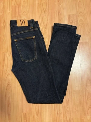 Nudie Jeans Grim Tim Dry Navy 30/32 - Säljer ett par mörkblå Nudie Jeans Grim Tim i modellen Dry Navy. Jeansen har klassisk femficksdesign, kontrastsömmar och är tillverkade av 99% ekologisk bomull och 1% elastan för lite stretch. Passformen är slim med raka ben och normal midja. Sprillans nya.