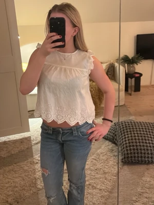 Vit blus med broderade detaljer - Säljer en söt vit blus med broderade hålmönster och volangkant nertill. Blusen är ärmlös med små volanger på axlarna och har en luftig, croppad passform. Köptes på only men tyvärr är inte lappen kvar. 