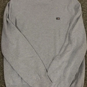 Ljusgrå stickad tröja från Lexington - Säljer en ljusgrå stickad tröja från Lexington med diskret logga på bröstet. Tröjan har rund halsringning, långa ärmar och ribbade muddar vid ärmslut och nederkant. Perfekt för dig som gillar klassisk och enkel stil. Köpte för 899 kronor hos kidsbrandstore och har inte använd tröjan en ända gång. Storleken ör ungefär S-M