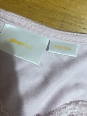 Ljusrosa långärmad topp Gina Tricot - Söt ljusrosa långärmad topp från Gina Tricot med v-ringning och spetsdetaljer runt halsen. Tillverkad i mjuk bomull som känns skön mot huden. Perfekt för dig som gillar en feminin och enkel stil.