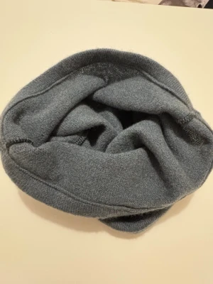 Blå Kashmir buff  - Mjuk och enkel grå halsvärmare i stickad ullmix. Modellen är tubformad och har en diskret, minimalistisk look utan detaljer eller mönster. Perfekt för att hålla värmen under kyliga dagar.