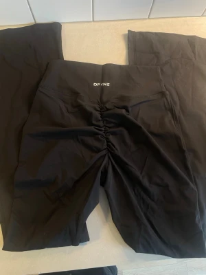 Svarta leggings från DFYNE - Storlek L  Säljer ett par svarta leggings från DFYNE med hög midja och snygg scrunch-detalj bak. De är tighta och gjorda i ett stretchigt syntetmaterial som passar perfekt för träning. Loggan sitter framtill på linningen och designen är stilren.