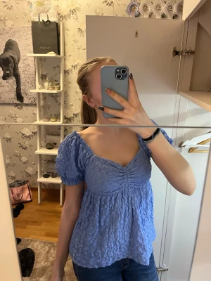 Ljusblå blus med puffärmar och snörning - Supersöt ljusblå blus med puffärmar och v-ringning. Blusen har en rynkad struktur och öppen rygg med snörning som detalj. Säljs då den inte kommer till användning längre!