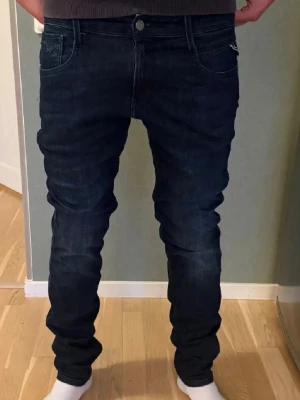 Mörkblå Replay anbass jeans slim fit - Säljer ett par mörkblå jeans från Replay med klassisk femficksdesign och snygga kontrastsömmar. Jeansen har slim passform, normal midja och är tillverkade i stretchigt jeansmaterial för extra komfort. Märkespatch bak i midjan och Replay-logga vid fickan.