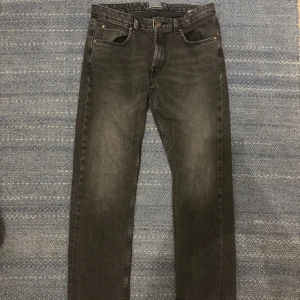 Svarta jeans från Dressmann 34/30 - Svarta jeans från Dressmann i regular fit med klassisk femficksdesign. Jeansen har en lätt tvättad look och raka ben. Tillverkade i bomull med en skön känsla och snygga detaljer vid fickor och midja.
