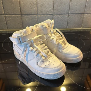 Nike Air Force 1 vita high sneakers - Klassiska Nike Air Force 1 high sneakers i helvitt skinn med snörning och kardborreband runt ankeln. Skorna är i eu 38, skriv vid funderingar  