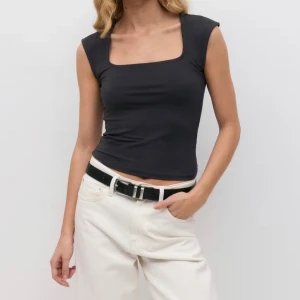 Svart croppad linnetopp med fyrkantig ringning - Svart croppad linnetopp med snygg fyrkantig ringning och breda axelband. Toppen är figurnära och har en enkel, stilren look som passar perfekt till jeans eller kjol. Tillverkad i mjukt och stretchigt material för en bekväm känsla.