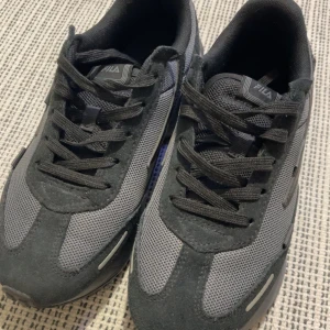 Mörkblå/svarta sneakers från Fila - Säljer ett par mörkblå/svarta Fila sneakers med chunky sula och cool mesh- och mockadetaljer. Skorna har snörning och Fila-logga på sidan, plösen och hälen. Perfekta för dig som gillar sportig och street-inspirerad stil. Använd 3 gånger, säljs då dom är försmå för mig. 