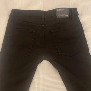 Svarta slim fit jeans Jack & Jones - Svarta slim fit jeans från Jack & Jones i modellen Glenn Original. Klassisk femficksdesign, smal passform och normal midja. Jeansen är tillverkade i bomull med en liten mängd stretch för extra komfort. Perfekta för en clean och stilren look.