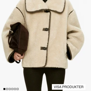 Beige teddyjacka med stora knappar - Säljer en beige teddyjacka med oversized krage och kontrasterande mörkbruna detaljer längs kanterna. Jackan har stora knappar framtill och en loose passform som ger en chill vibe. Perfekt för kalla dagar när du vill vara både varm och snygg. Helt oanvänd med prislappen kvar. Nypris:2290