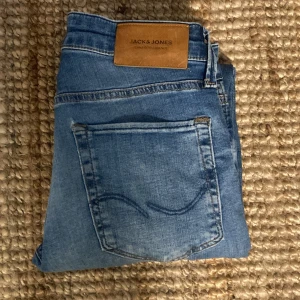 Blå slim jeans från Jack & Jones - Snygga blå jeans från Jack & Jones, modell Slim/Glenn. Jeansen har klassisk femficksdesign, normalhög midja och smal passform. Tillverkade i mjukt denimtyg med lätt slitningar och snygg tvätt. Perfekta för en avslappnad och trendig look.