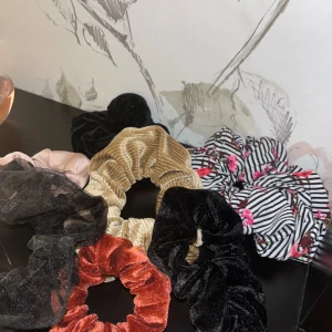 Mixade scrunchies i olika färger - Säljer ett gäng scrunchies i olika material och färger. Du får en beige manchester, svart och röd sammet, svart mesh med prickar, ljusrosa satin och en randig vit/svart med blommor. Perfekt för att piffa upp din frisyr med coola detaljer.