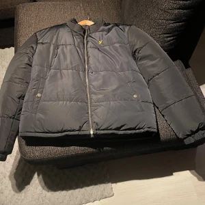 Vändbar svart/grå pufferjacka Lyle & Scott - Vändbar pufferjacka från Lyle & Scott i svart på ena sidan och grått mönster med små prickar på andra. Jackan har dragkedja, ståkrage och två fickor med tryckknapp eller dragkedja beroende på sida. Perfekt för dig som vill variera din stil. Jackan är nästan aldrig använd och nypriset ligger på 2800kr men mitt pris är 1300kr