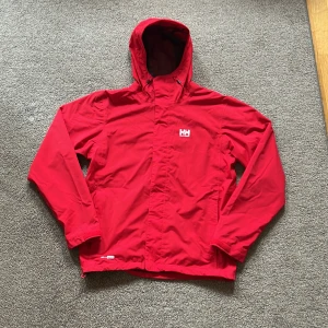 Röd Helly Hansen vindjacka S - Riktigt snygg röd vindjacka från Helly Hansen med Helly Tech-tyg. Den är i storlek S och sitter riktigt bra. Vattentät & vindtät för en kyligare höstmånad. Justerbar midja. Mycket bra skick på jackan. Fraktas samma dag som köp🚚💨