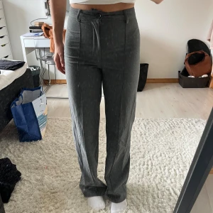 Grå kostymbyxor med hög midja - Grå kostymbyxor med hög midja och raka ben. Byxorna har pressveck framtill, bälteshällor samt knapp och dragkedja. Materialet känns mjukt och följsamt. Från pull&bear, storlek S men ganska små i storleken, skulle säga närmre xs eller kanske för dig som är lite mitt emellan.