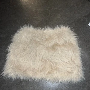 Beige fluffig päls-tubtopp - Supercool beige kjol i fuskpäls med fluffig känsla. Perfekt för dig som vill sticka ut och skapa en statement-look. Toppen är axelbandslös och har en mjuk, mysig yta som känns lyxig och trendig.