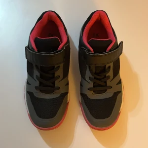 Svarta sneakers med grå detaljer stl 35 - Snygga svarta sneakers från SOC i storlek 35 med grå detaljer och rosa foder. Skorna har både snörning och kardborreband för extra bra passform. Ovandelen är i syntet och mesh för bra andningsförmåga. Perfekta för dig som gillar sportig stil.