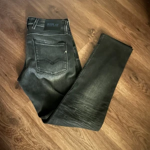 Replay anbass gråa jeans - Säljer ett par gråa Replay anbass jeans med snyggt slitna detaljer och klassiska bakfickor. Jeansen har raka ben och slim passform, perfekt till dig som gillar en stilren look. Materialet är jeans och färgen är mörkgrå till svart.