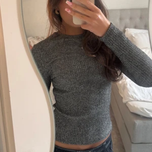 Grå ribbad långärmad tröja - Säljer en grå ribbad långärmad tröja med rund halsringning. Tröjan har en slim passform och är tillverkad i ett mjukt, stretchigt material som sitter snyggt på kroppen. Perfekt att styla med jeans eller kjol för en enkel och clean look.