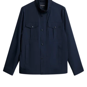 Marinblå overshirt från J.Lindeberg - Snygg marinblå overshirt från J.Lindeberg med raka linjer och stilrena fickor med knappar på bröstet. Jackan har lång ärm, klassisk krage och stängs med knappar framtill. Perfekt för dig som gillar minimalistisk och clean stil. Nypris är ca 3499 och den är använd i ett halvår.