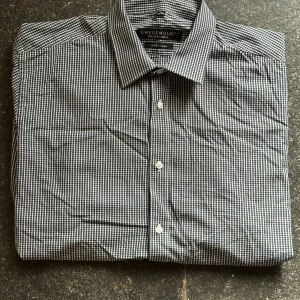 Rutig skjorta från Swedemount - Snygg rutig skjorta från Swedemount i mörkblått och vitt. Klassisk krage, knäppning framtill och långa ärmar med manschett. Skjortan är i bomull och har en stilren, tidlös look som passar till många olika outfits.