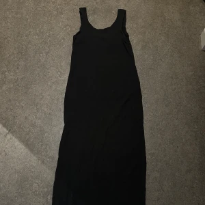 Svart långklänning med breda axelband - En stilren svart långklänning med breda axelband och rundad halsringning. Klänningen har en rak och enkel siluett som ger en clean look. Den har en slits om vänster ben också, svårt o få på bild. Storlek S men är som en M/L Säljer för 50kr