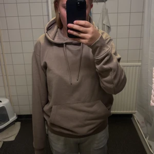 Beige hoodie från Revival  - Säljer en beige hoodie från Revival i storlek S. Tröjan har huva med snörning, stor magficka och ribbade muddar. Mjuk insida och klassisk passform, perfekt för chill dagar. Enkel och stilren design utan tryck eller mönster.