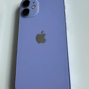 iPhone 12 mini - Snygg lila iPhone 12 i mycket gott skick, utan synliga repor eller skador. Levereras med originalkartong och flera roliga och färgglada skal. Dubbelkamera, Face ID och modern design. Perfekt för dig som vill ha en pålitlig och stilren mobil med extra tillbehör.