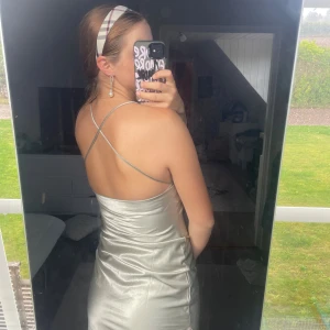 Ljusgrön silvrig långklänning med tunna band - Supersnygg långklänning i ljusgrönt silvrigt satinliknande material med tunna axelband som korsas i ryggen. Klänningen har en draperad urringning och öppen rygg för en riktigt elegant vibe. Perfekt för dig som vill sticka ut med en glansig look.☘️✨