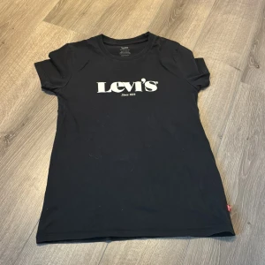 Levi's t-shirt - Svart t-shirt från Levi's med klassisk vit logga på bröstet. Modellen är kortärmad och har en rund halsringning. Tillverkad i mjuk bomull som känns skön mot huden. Perfekt för en avslappnad och stilren look. Lite ludd på den då den legat mot en stickad tröja😅Knappt använd!