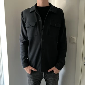 Mörkblå overshirt - Stilren blå overshirt med klassisk krage och knäppning framtill. Två bröstfickor med lock och knappar ger en clean look. Långärmad modell i ett mjukt material som passar perfekt till jeans. Enkel och snygg att styla till olika outfits. 