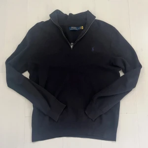 Mörkblå half zip från Ralph Lauren - Mörkblå stickad tröja från Polo Ralph Lauren med half zip-dragkedja och broderad logga på bröstet. Finns ett litet hål på ryggen, går lätt och sy ihop. Annars fint skick.