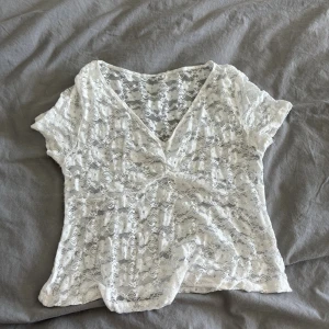 Vit spetsblus med v-ringning - Säljer en superfin vit blus i spets med v-ringning och korta ärmar. Blusen är genombruten med blommigt spetsmönster och har en lätt croppad passform. Perfekt att styla över ett linne eller bralette för en trendig look. Storlek L men sitter som M