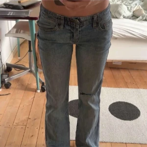 Blå bootcut jeans med slitning - Snygga blå jeans med bootcut passform och låg midja. Jeansen har klassisk femficksdesign, slitning på ena knät och lätt tvättad look. Perfekta för dig som gillar en avslappnad och trendig stil.