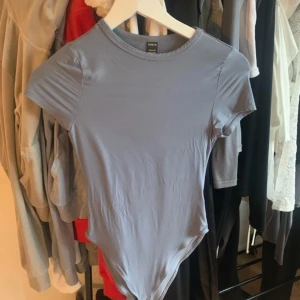 Ljuslila kortärmad bodysuit från SHEIN - En stilren ljuslila bodysuit från SHEIN med rund halsringning och korta ärmar. Tight passform som sitter snyggt mot kroppen. Perfekt att styla med jeans eller kjol för en clean look.
